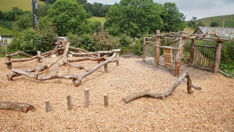 Play area with a climbing frame made out of logs